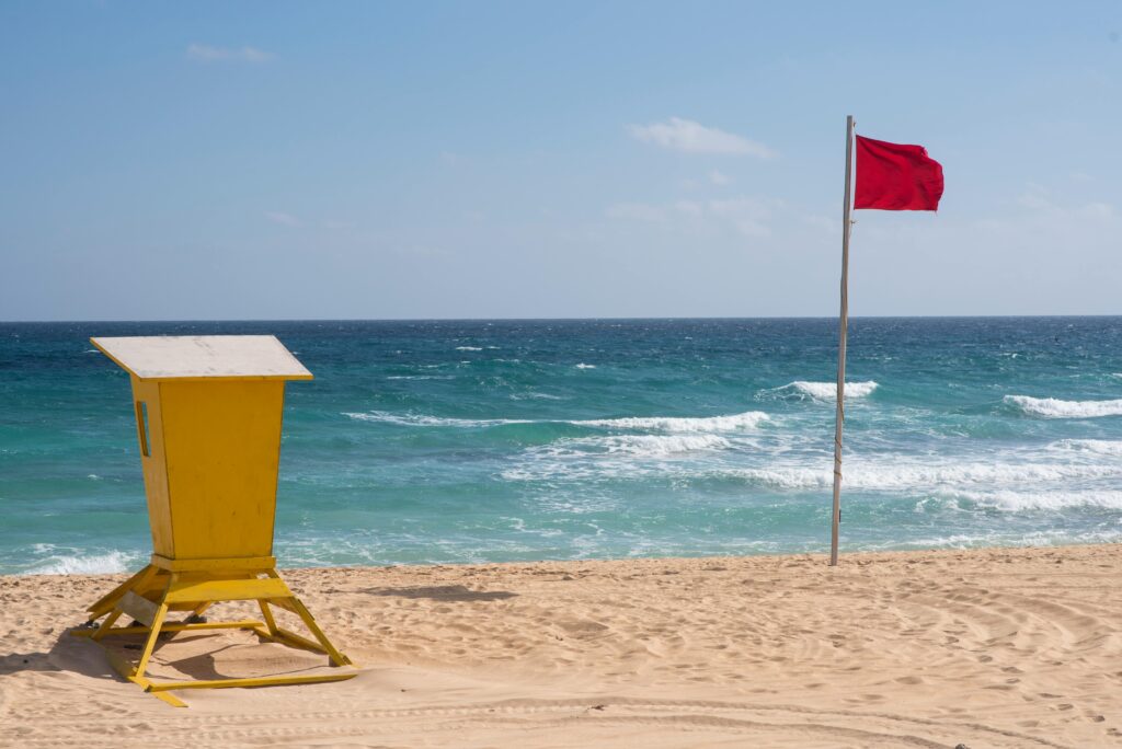 Beach scene with lifeguard station and red flag warning against strong waves.