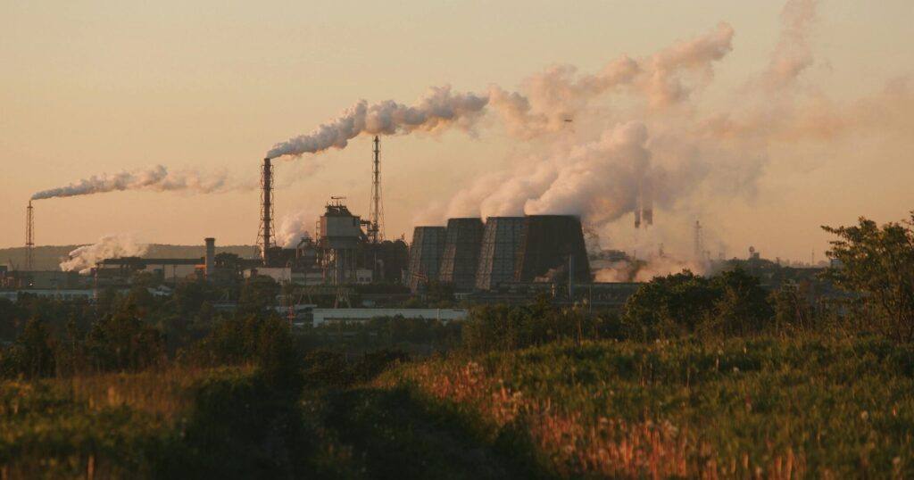 Factory chimneys releasing smoke into the sky at sunset, highlighting industrial pollution.