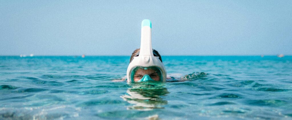 A snorkeler with a mask in the clear blue sea, enjoying a sunny day underwater.