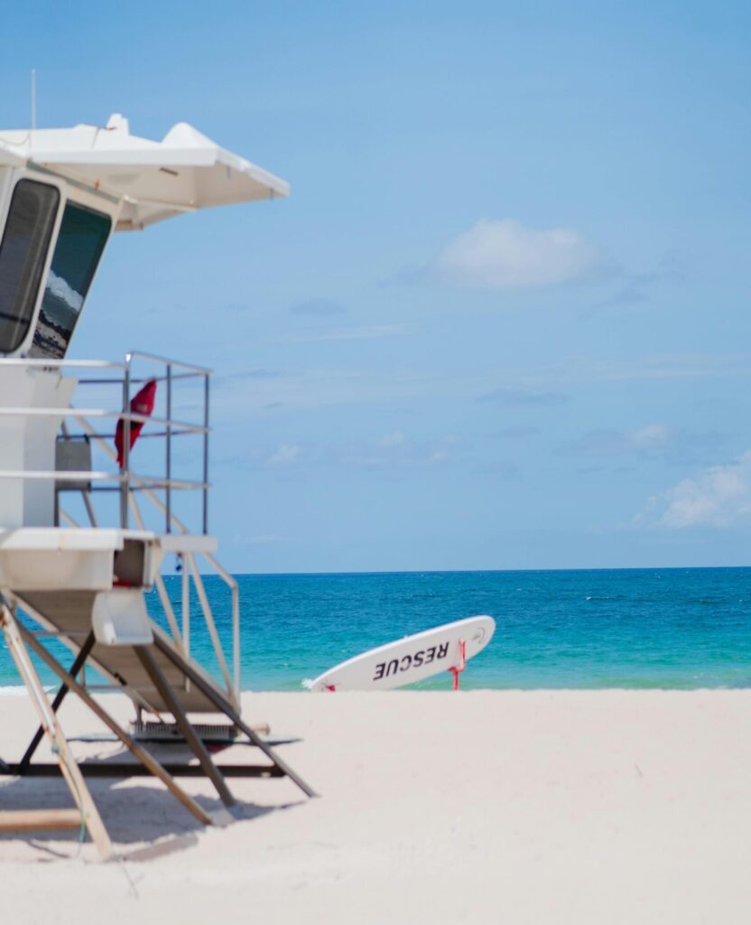 A lifeguard tower and rescue board on a sandy beach by the turquoise sea under a clear blue sky.