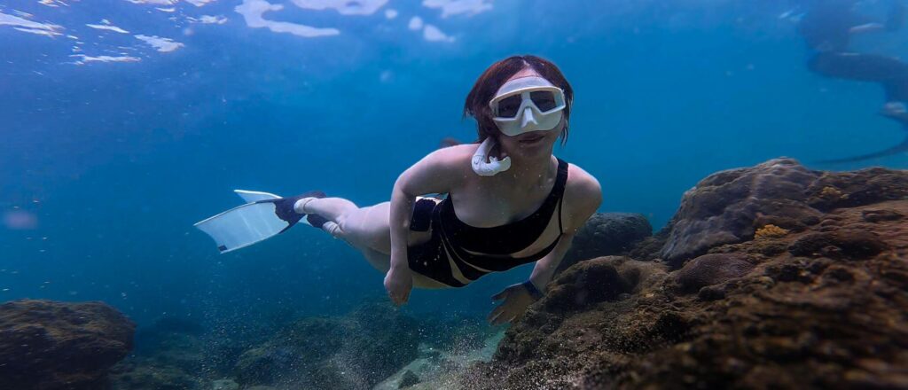 Explore serene underwater world with a woman snorkeling near vibrant coral reefs.
