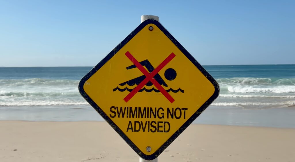 Warning sign on Byron Bay beach advising against swimming due to safety concerns.