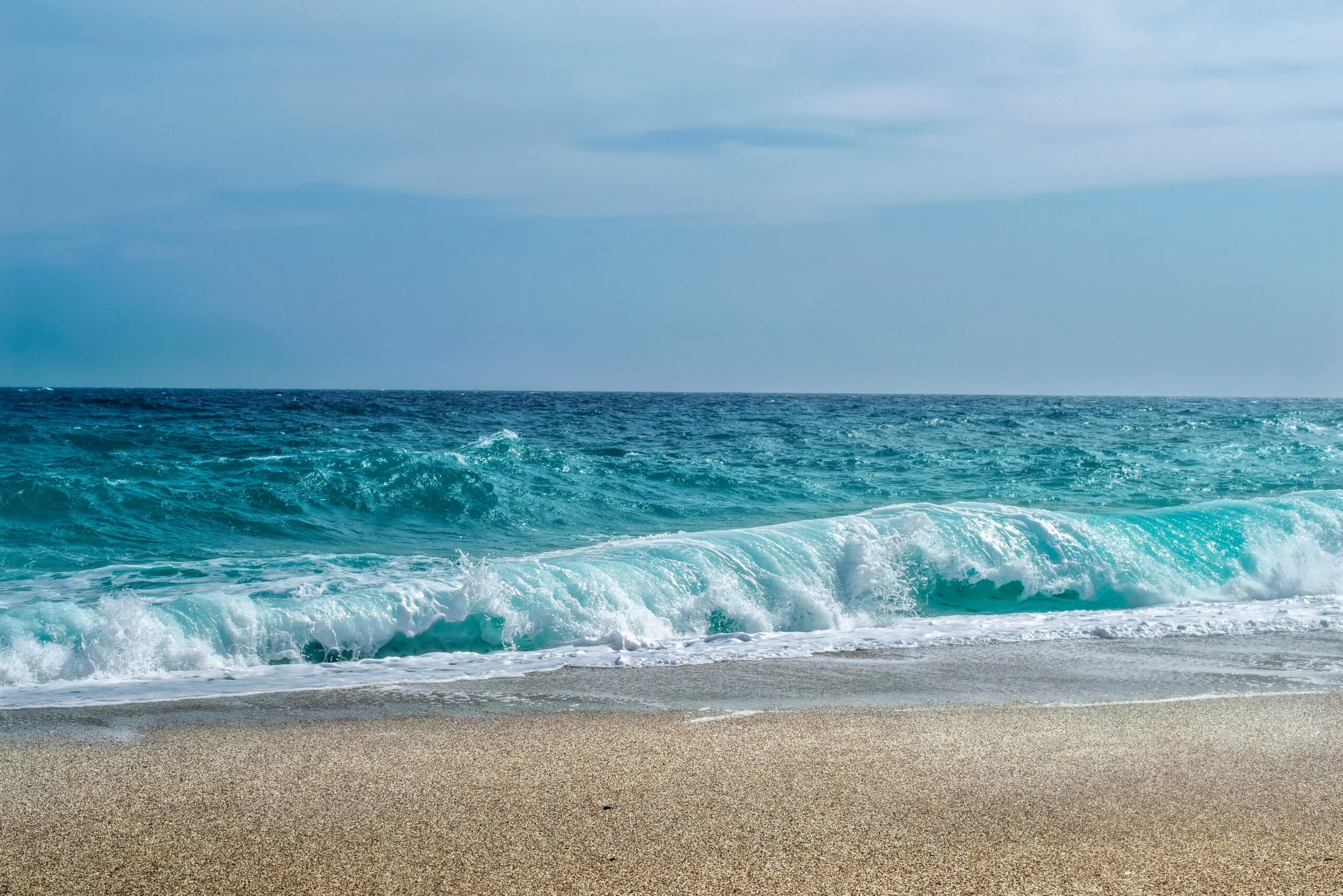 Stunning view of turquoise ocean waves crashing onto a sandy shore under a clear sky.