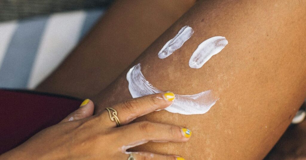 Close-up of a hand applying sunscreen on a leg with a smiley. Sunny and fun outdoor setting.