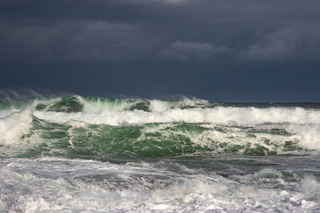 Powerful ocean waves crash under dark stormy clouds, capturing nature's raw force.