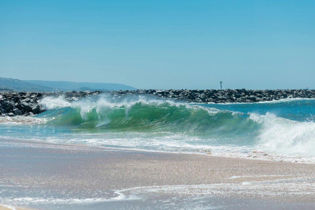 A picturesque ocean wave crashes on a sunny beach with clear blue skies.