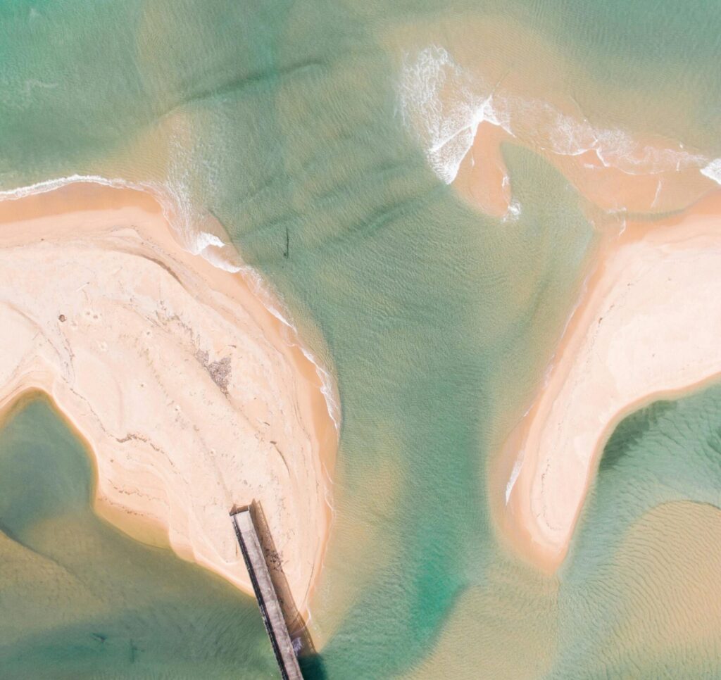 Aerial shot of a tropical beach with a wooden pier and shimmering sandbanks.